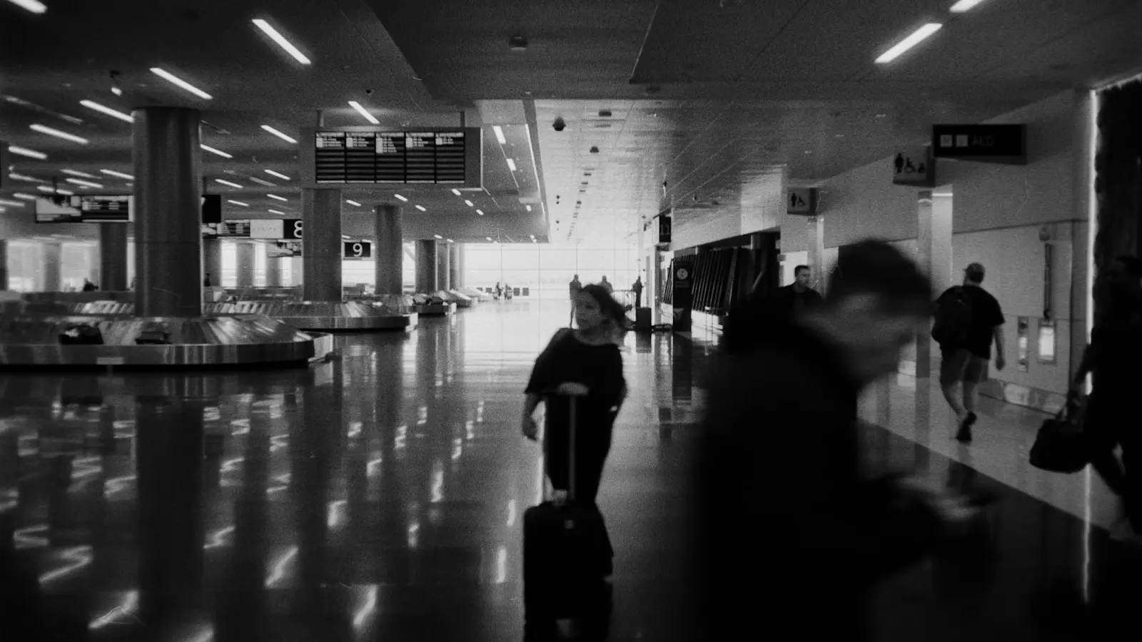 Travelers pulling wheeled suitcases through an airport terminal near the baggage carousels