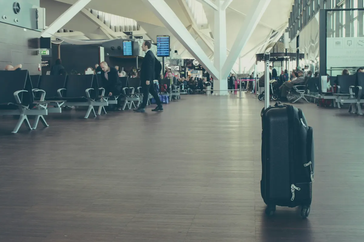 A traveler standing with a wheeled carry-on suitcase inside an airport terminal